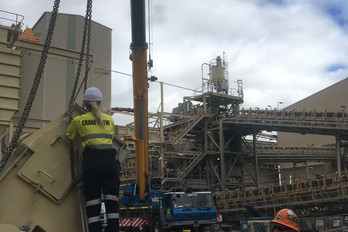 A rigger on a ladder slinging a load, an all-terrain crane set up behind